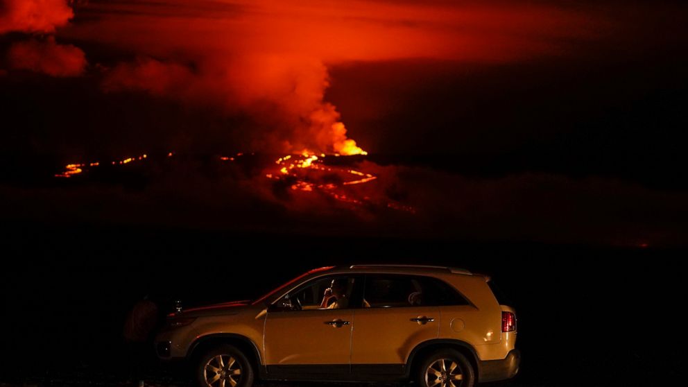 A man talks on a phone in his car alongside Saddle Road as the Mauna Loa volcano erupts Wednesday, Nov. 30, 2022, near Hilo, Hawaii. Hundreds of people in their cars lined Saddle Road, which connects the east and west sides of the island, as lava flo