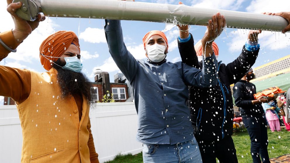 Jasbir Singh, left, and Vijay Singh wash a flagpole with milk as part of a ceremonial changing of the Sikh flag during Vaisakhi celebrations at Guru Nanak Darbar of Long Island, Tuesday, April 13, 2021 in Hicksville, N.Y. Sikhs across the United Stat