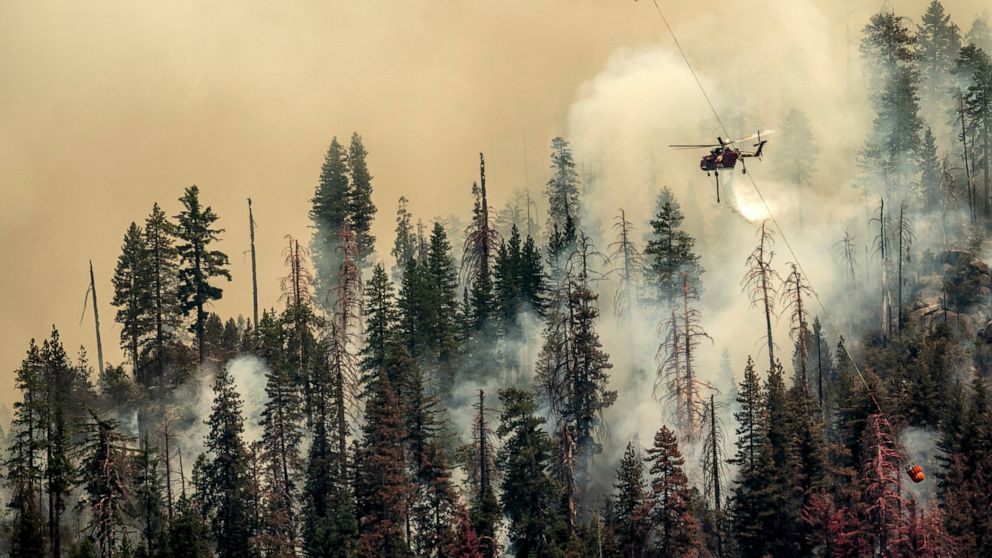 Seen from unincorporated Mariposa County, Calif., a helicopter drops water on the Washburn Fire burning in Yosemite National Park on Saturday, July 9, 2022. (AP Photo/Noah Berger)