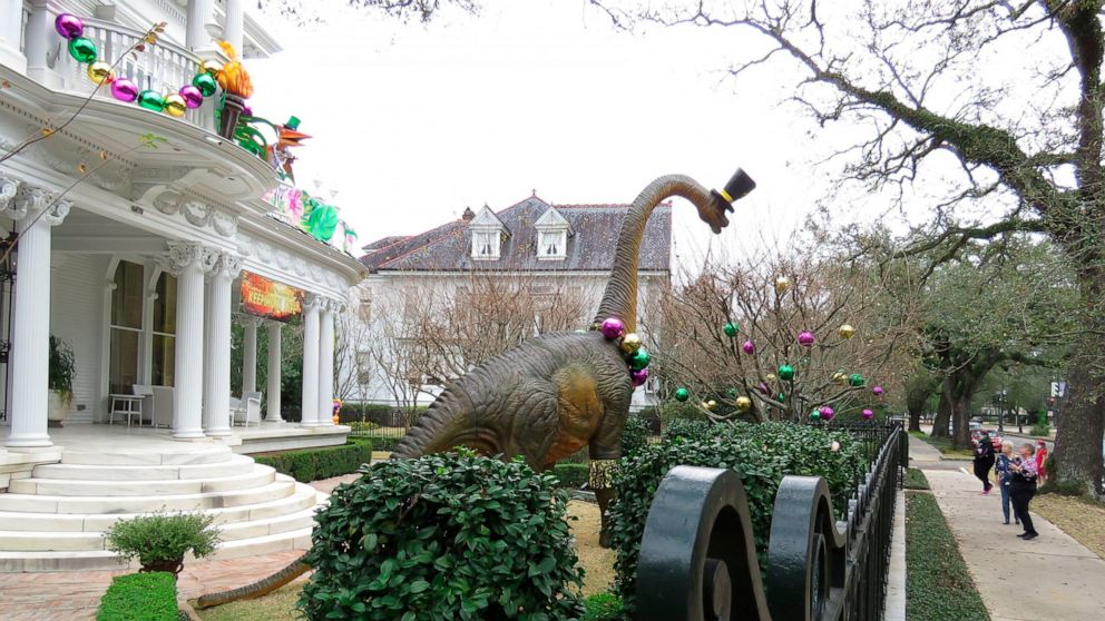 FILE - In this Tuesday, Jan. 26, 2021, file photo, passersby look at dinosaurs on the balcony of a mansion on St. Charles Avenue in New Orleans. The banner says "Thank you, Mayor, for keeping us safe." The group behind the wave of houses decorated to