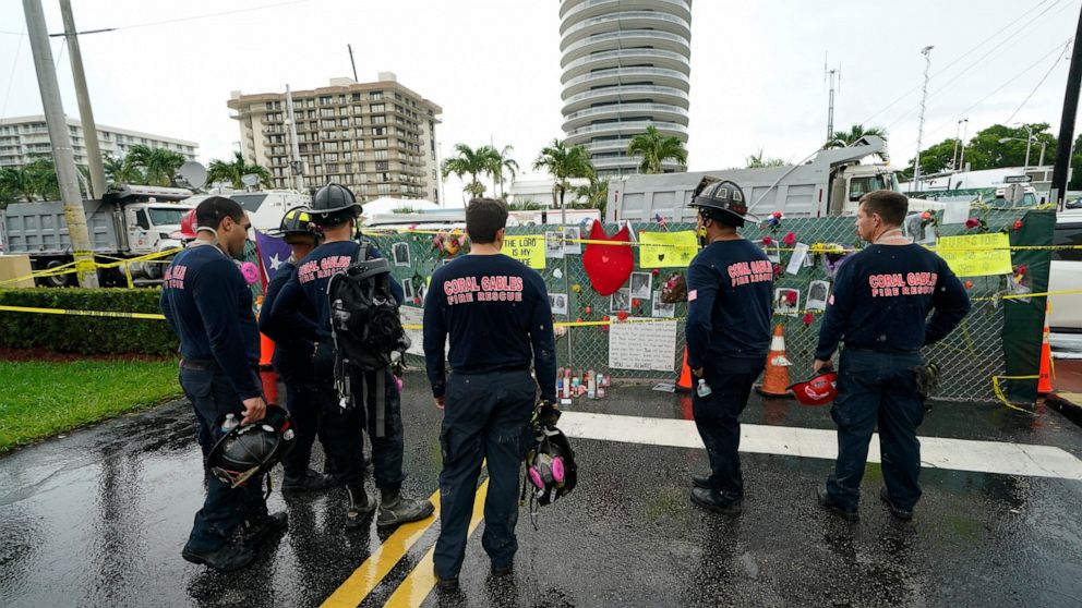 Members of the Coral Gables Fire Department pay their respects at a makeshift memorial to the people killed and the scores who remain missing, nearly a week after the partial collapse of the Champlain Towers South condo building, the remaining sectio