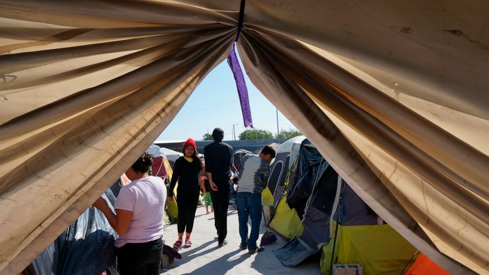 Migrants walk by their tents in the Senda de Vida 2 shelter in Reynosa, Mexico, Thursday, Dec. 15, 2022. Nearly three thousand people cram inside the vast compound of tents over cement or gravel by the Rio Grande, steps from the border with the Unite