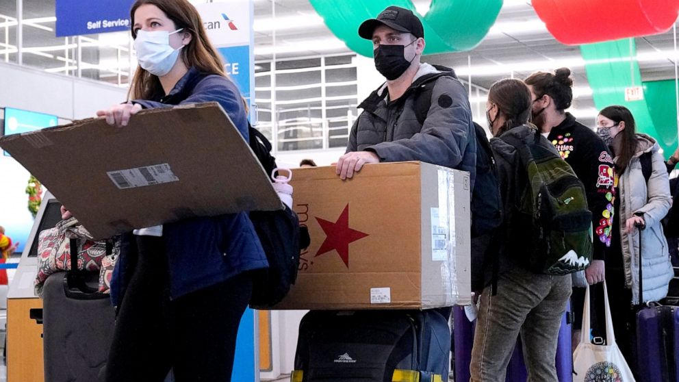 FILE - Travelers line up wearing protective masks indoors at O'Hare International Airport in Chicago, Tuesday, Dec. 28, 2021. Illinois Gov. J.B. Pritzker said Wednesday, Feb. 9, 2022, that at the end of the month he will lift the requirement for face
