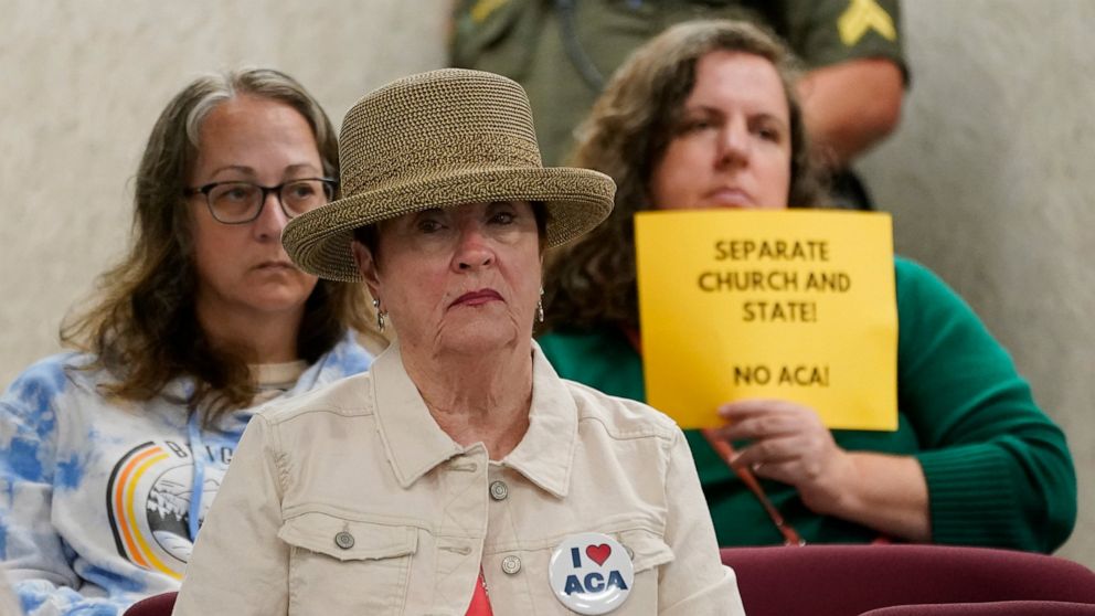 FILE - A woman wearing a button supporting charter schools linked to Hillsdale College sits in front of a woman holding a sign opposing the schools during a meeting of the Tennessee Public Charter School Commission staff on Sept. 14, 2022, in Murfree
