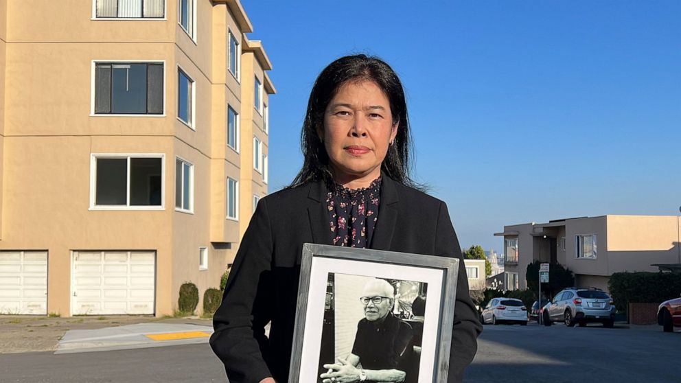 Monthanus Ratanapakdee holds a photo of her father, 84-year-old Vicha Ratanapakdee, and stands in front of the San Francisco apartment building where he was attacked last year and later died of his injuries, on Jan. 26, 2022. On Sunday, Jan. 30, 2022