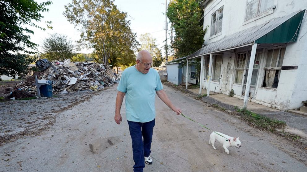 Tommy Goodwin walks his dog, Tasha, down a street lined with flood-damaged buildings and piles of debris Sept. 27, 2021, in Waverly, Tenn. After a devastating flood hit Aug. 21, the town of just over 4,000 people faces a dilemma. More than 500 homes 