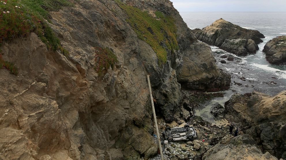 Bodega Bay firefighters work to secure the scene of a crash after a vehicle plummeted from the Bodega Head parking lot in Bodega Bay, Calif., through a wood barrier, left, landing upside down 100 feet to the rocky shoreline, killing two people in the