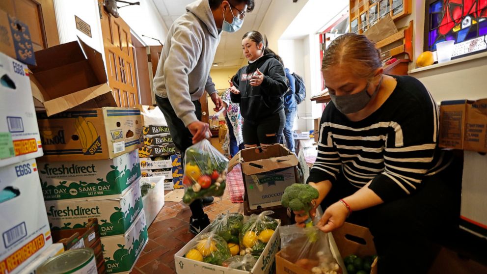 FILE - In this Tuesday, May 12, 2020 file photo, Laura Porras, right, prepares bags of fresh vegetables as Justin Ruiz, 17, left, and Porras' niece Ana Karen Porras, 14, help in the vestibule at Lutheran Church of the Good Shepherd in the Bay Ridge n
