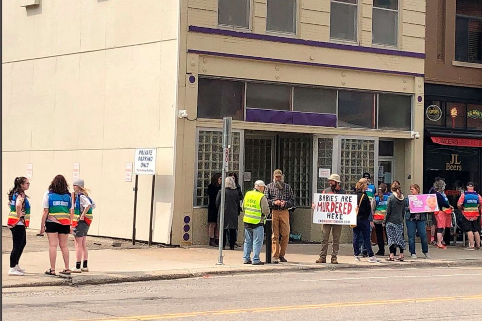 PHOTO: In this May 11, 2022, file photo, protesters at North Dakota's lone abortion clinic are flanked by patient escorts in rainbow-colored vests, in Fargo, N.D.