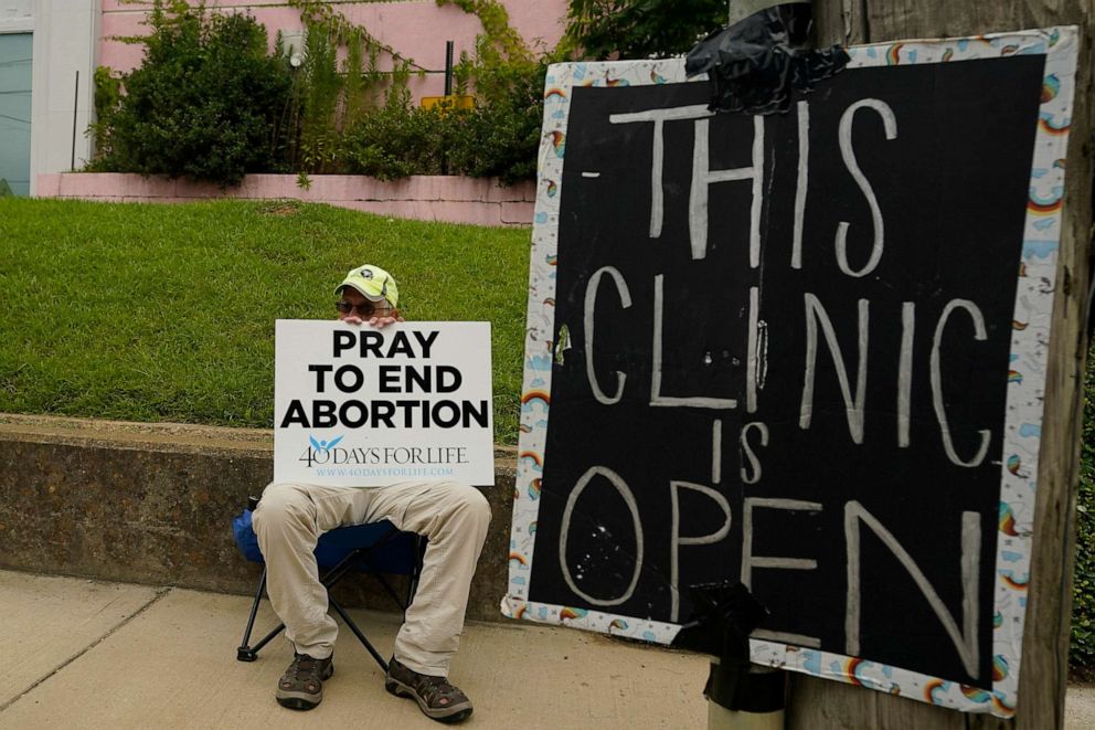 PHOTO: An anti-abortion supporter sits behind a sign that advises the Jackson Women's Health Organization clinic is still open in Jackson, Miss., Wednesday, July 6, 2022.
