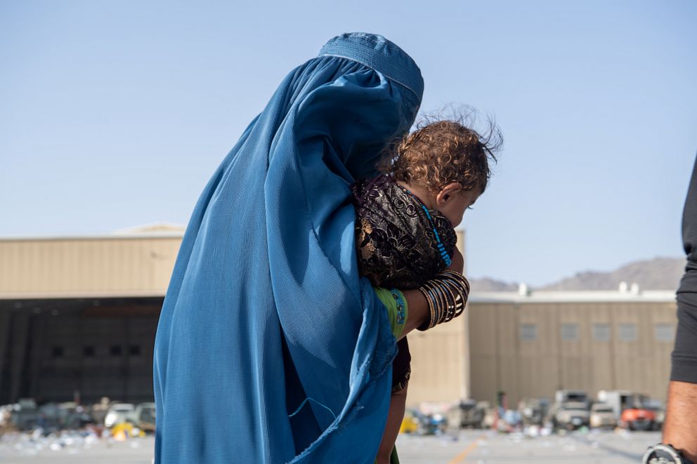 PHOTO: A woman carries a child as passengers board a plane to evacuate at Hamid Karzai International Airport in Kabul, Afghanistan, Aug. 24, 2021.