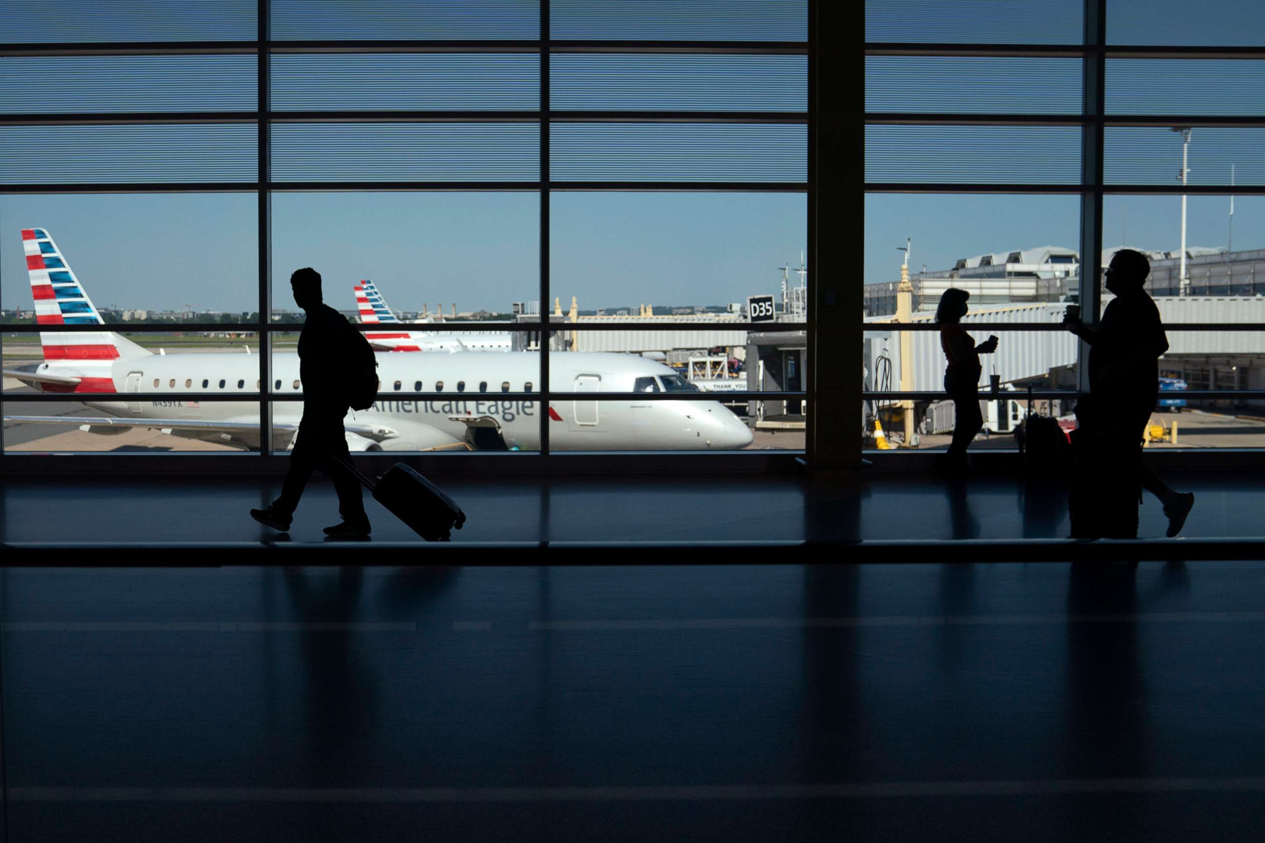 PHOTO: Travelers walk past planes gated at Ronald Regan Washington National Airport on July 11, 2022, in Arlington, Va. 