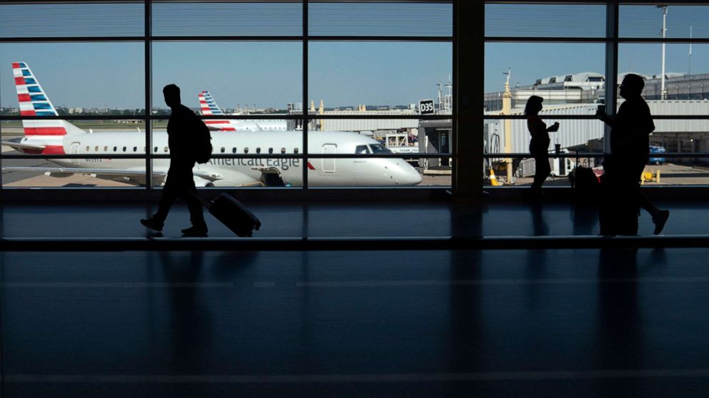 PHOTO: Travelers walk past planes gated at Ronald Regan Washington National Airport on July 11, 2022, in Arlington, Va. 