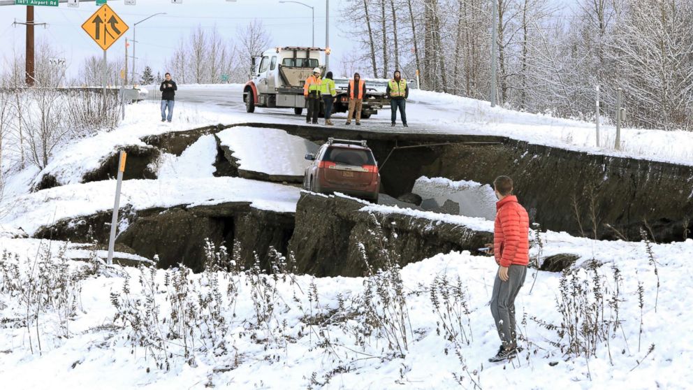 PHOTO: Highway workers and spectators look at a car stuck on a section of an off-ramp that collapsed during an earthquake in Anchorage, Ala., Nov. 30, 2018.
