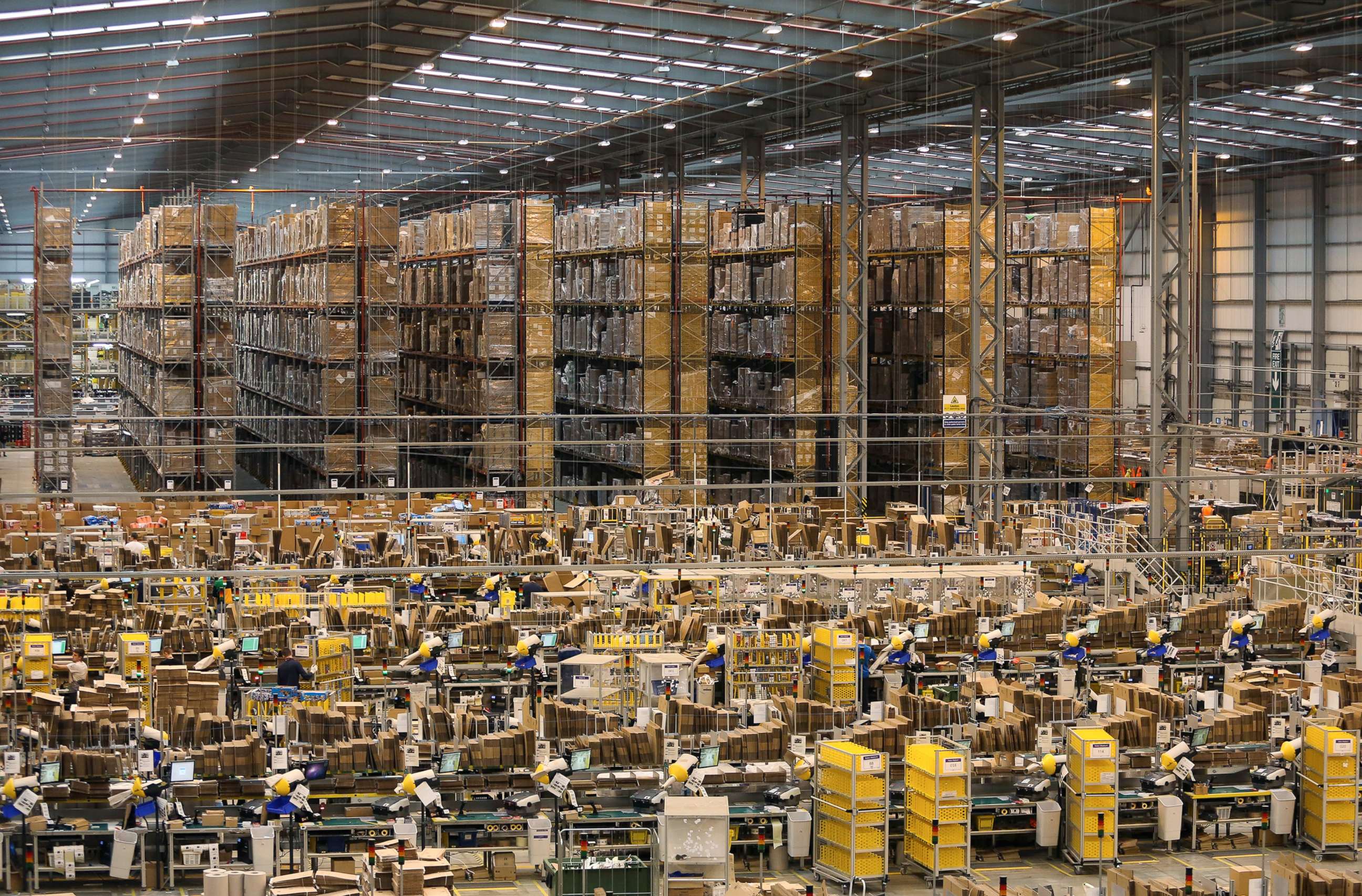 PHOTO: Storage racks stand beyond employees as they process customer orders at one of Amazon.com Inc.'s fulfillment centers in Peterborough, U.K., Nov. 25, 2014. 