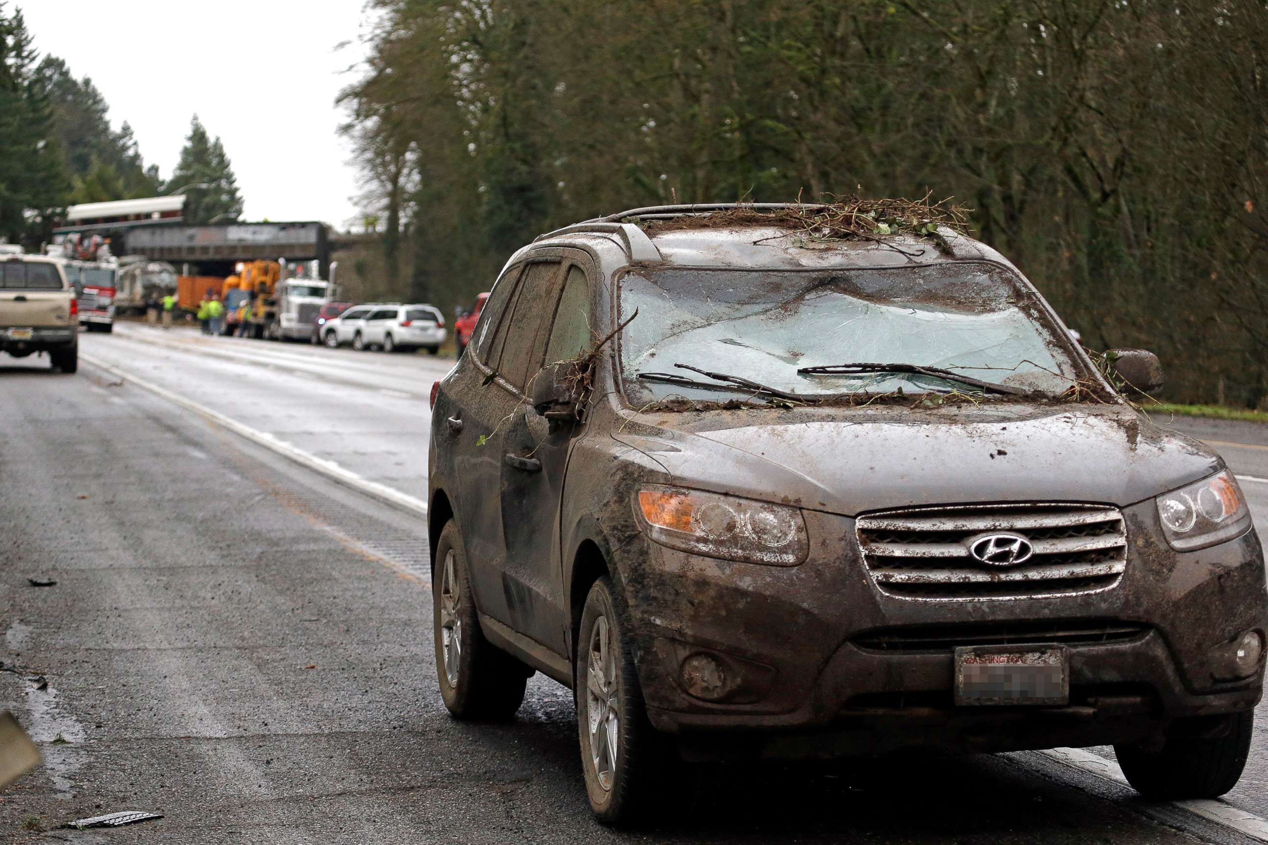 PHOTO: A car covered in mud and debris with a smashed windshield and other damage sits parked on the shoulder just beyond where an Amtrak train derailed onto Interstate 5, Dec. 18, 2017, in DuPont, Wash.