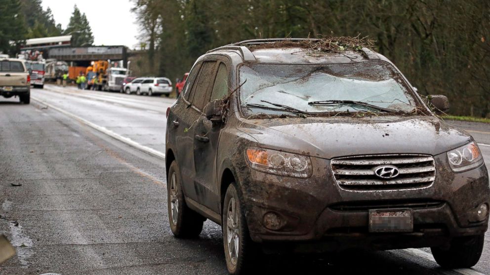 PHOTO: A car covered in mud and debris with a smashed windshield and other damage sits parked on the shoulder just beyond where an Amtrak train derailed onto Interstate 5, Dec. 18, 2017, in DuPont, Wash.