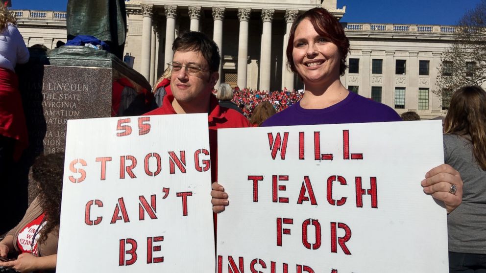 Teachers John and Kerry Guerini of Fayetteville, West Virginia, hold signs at a rally at the state Capitol in Charleston, W.Va., Monday, Feb. 26, 2018. Teachers across West Virginia will continue a walkout over pay and benefits for a fourth day.