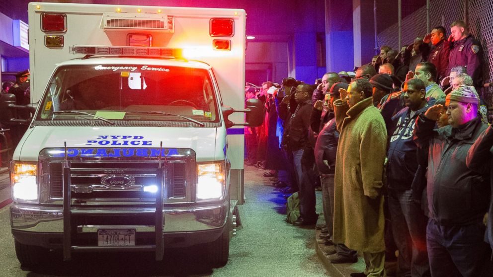 Mourners stand at attention as the bodies of two fallen NYPD police officers are transported from Woodhull Medical Center, Saturday, Dec. 20, 2014, in New York.  An armed man walked up to two New York Police Department officers sitting inside a patrol car and opened fire Saturday afternoon, killing both before running into a nearby subway station and committing suicide, police said.