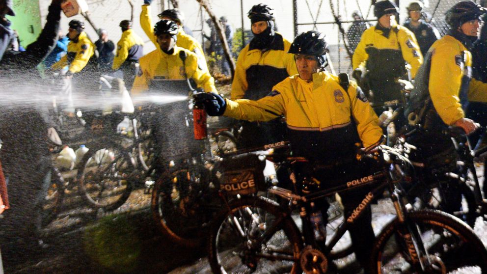A police officer sprays a liquid towards demonstrators at the Minneapolis Police Department 4th Precinct building, Nov. 18, 2015, in Minneapolis.