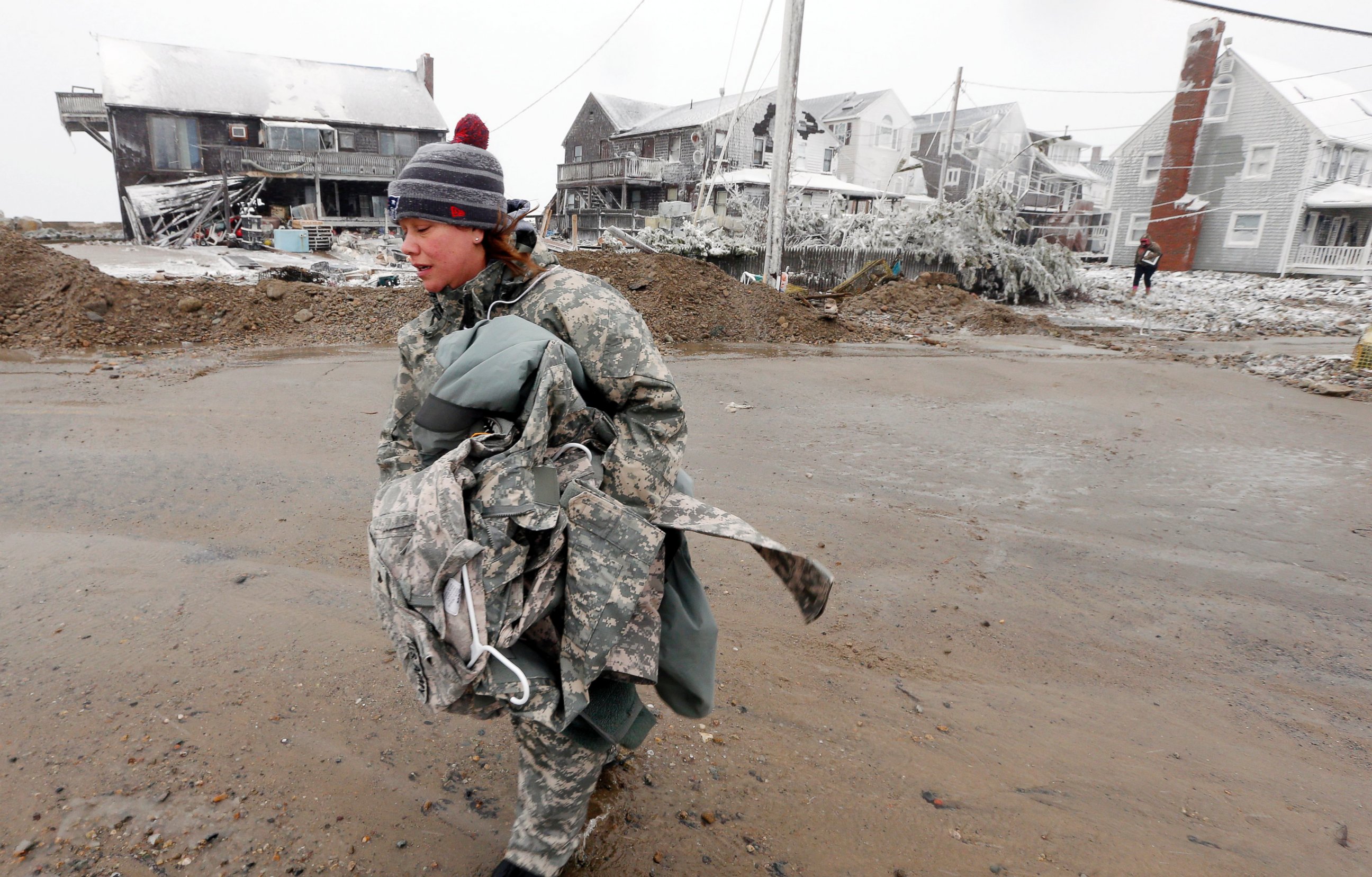 PHOTO: U.S. Army soldier Jennifer Bruno carries some belongings from her house, center rear, that was heavily damaged by storm surge during a winter storm, Jan. 27, 2015, in Marshfield, Mass. 