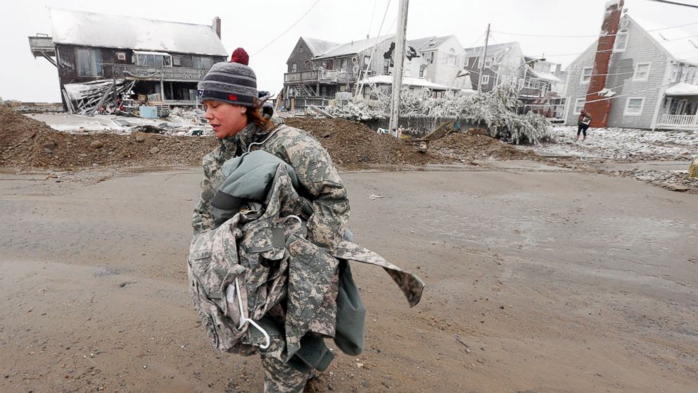 PHOTO: U.S. Army soldier Jennifer Bruno carries some belongings from her house, center rear, that was heavily damaged by storm surge during a winter storm, Jan. 27, 2015, in Marshfield, Mass. 
