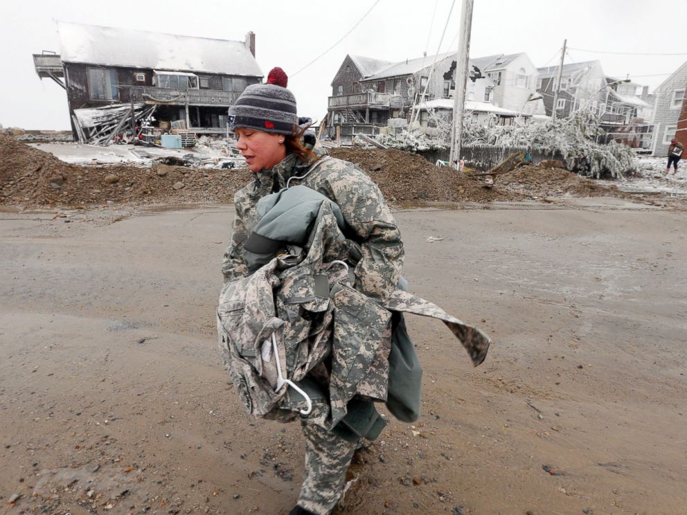 PHOTO: U.S. Army soldier Jennifer Bruno carries some belongings from her house, center rear, that was heavily damaged by storm surge during a winter storm, Jan. 27, 2015, in Marshfield, Mass.
