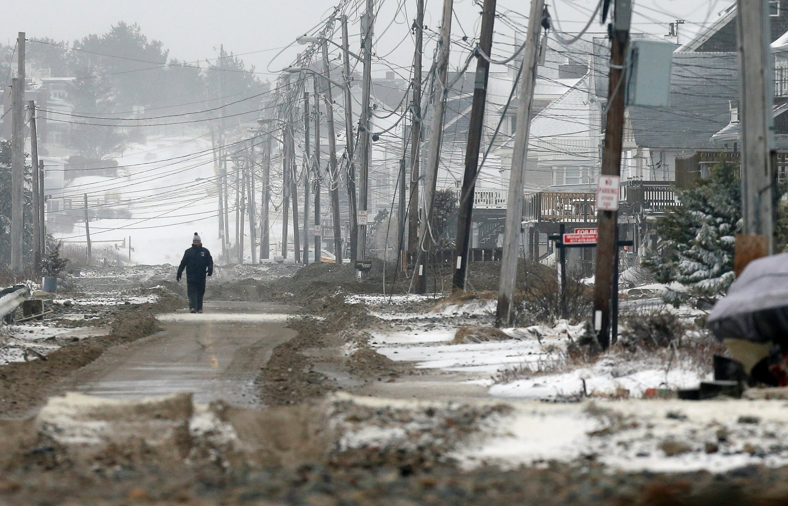 PHOTO: A man walks on a portion of road cleared of sand washed up by ocean waves during a winter storm in the Humarock section of Scituate, Mass., Jan. 27, 2015.