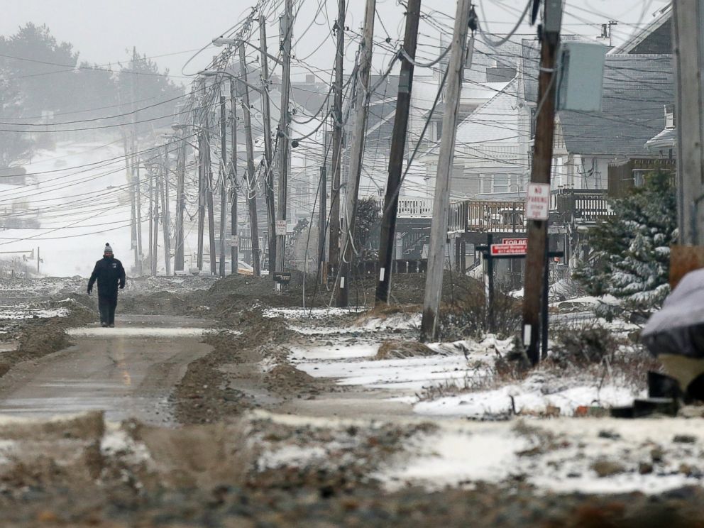 PHOTO: A man walks on a portion of road cleared of sand washed up by ocean waves during a winter storm in the Humarock section of Scituate, Mass., Jan. 27, 2015.