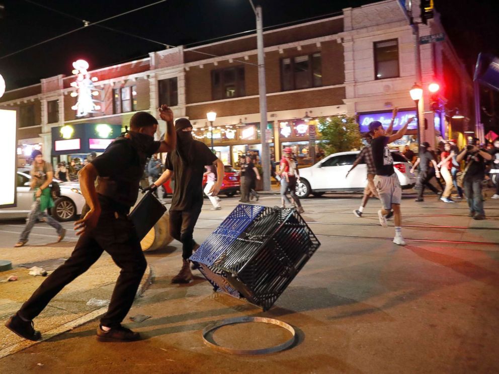 PHOTO: People overturn trash cans and throw objects as police try to clear a violent crowd Saturday, Sept. 16, 2017, in University City, Mo.