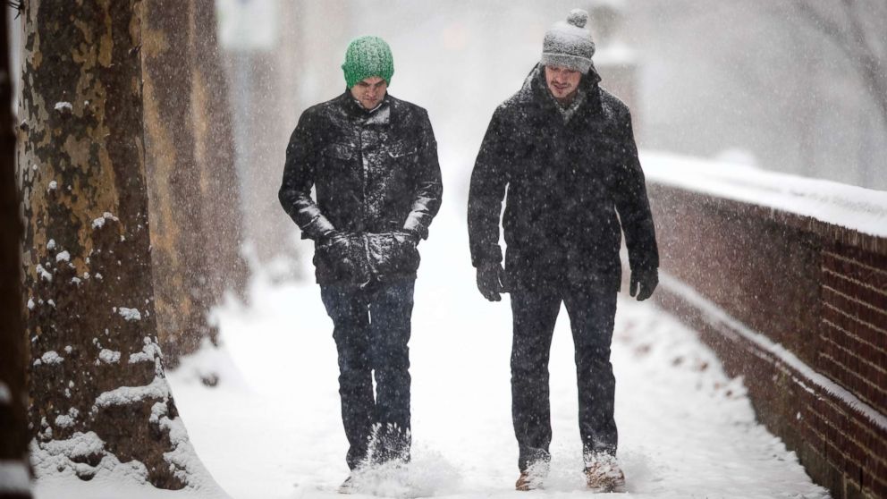 Men walk along a snow cover sidewalk during a storm in Philadelphia, Friday, Dec. 15, 2017.