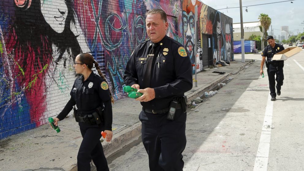 Miami police officer James Bernat, right, carries cans of mosquito spray as he walks in an area frequented by homeless people, Tuesday, Aug. 2, 2016 in the Wynwood neighborhood of Miami.
