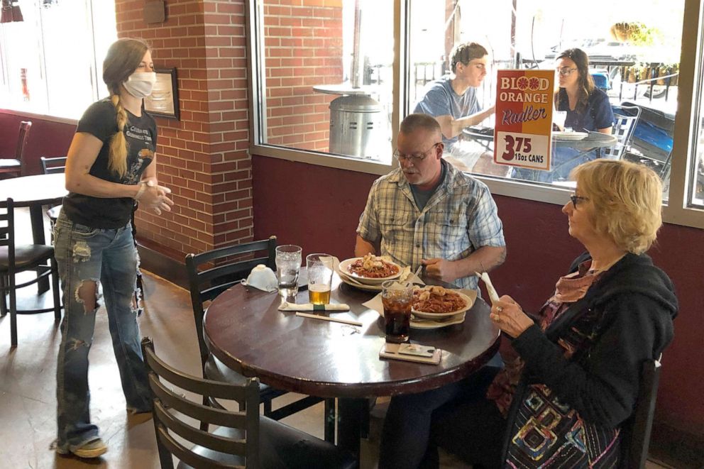 PHOTO: Anna Barnard, left, wears a protective mask as she talks to Greg and Judy Robinson at Dugan's Pub in Little Rock, Arkansas on Monday, May 11,2020.