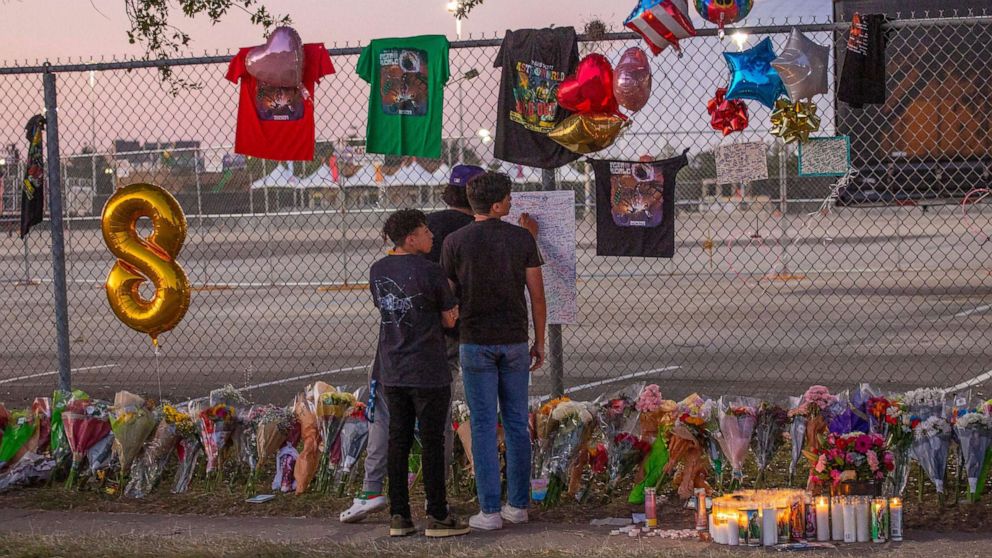 PHOTO: Local high School friends who attended the Travis Scott concert, Isaac Hernandez and Matthias Coronel watch Jesus Martinez sign a remembrance board at a makeshift memorial on Nov. 7, 2021, at the NRG Park grounds in Houston.