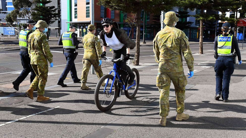 PHOTO: A cyclist passes a group of police and soldiers patrolling the Docklands area of Melbourne, Aug. 2, 2020, after the announcement of new restrictions to curb the spread of the COVID-19 coronavirus.