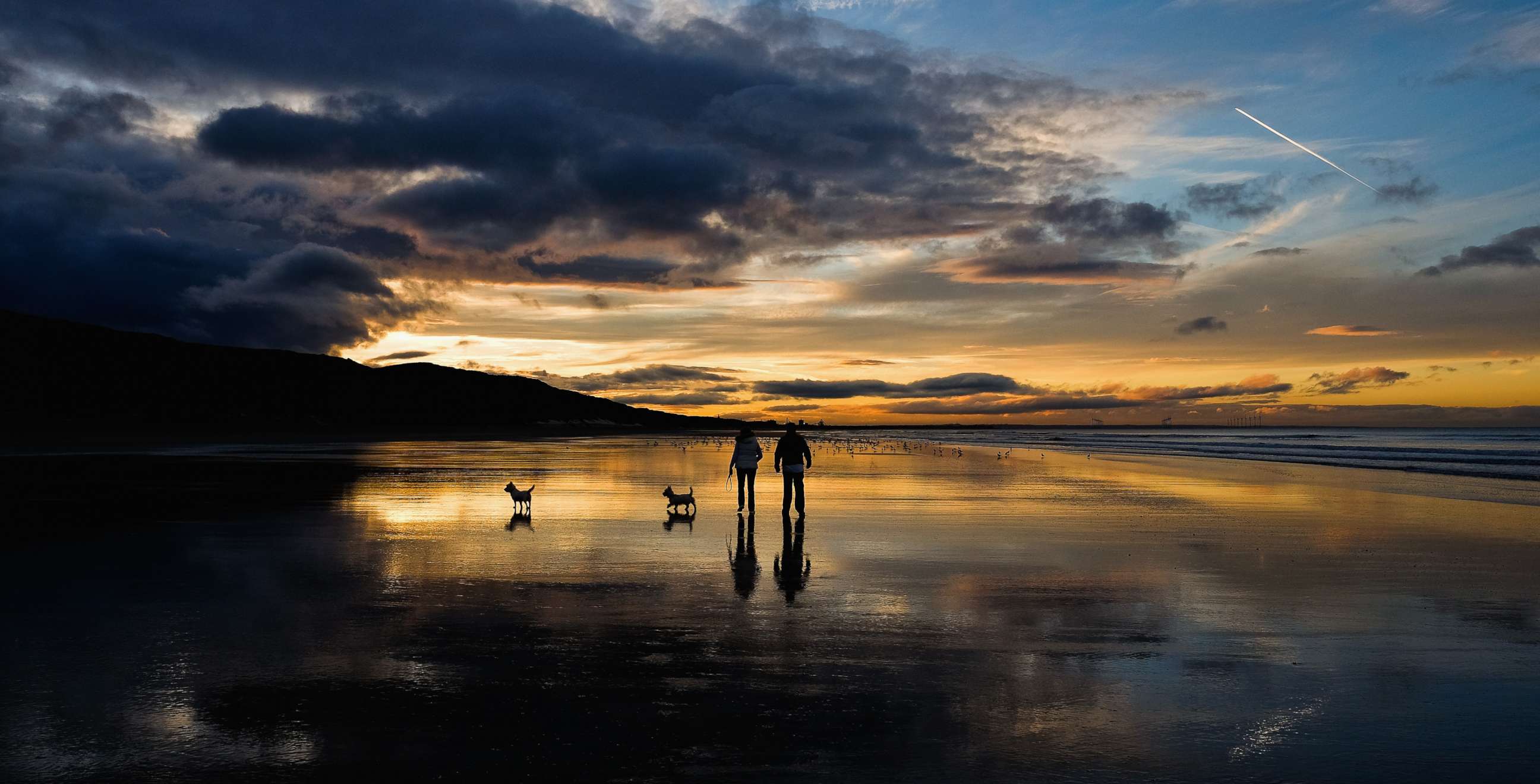 PHOTO: A couple walk their dogs on the beach as the sun sets on the Autumn Equinox, which marks the first day of Autumn, Sept. 23, 2015, in Saltburn, England.