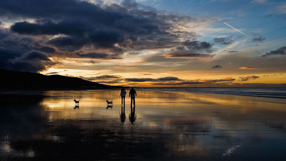 PHOTO: A couple walk their dogs on the beach as the sun sets on the Autumn Equinox, which marks the first day of Autumn, Sept. 23, 2015, in Saltburn, England.