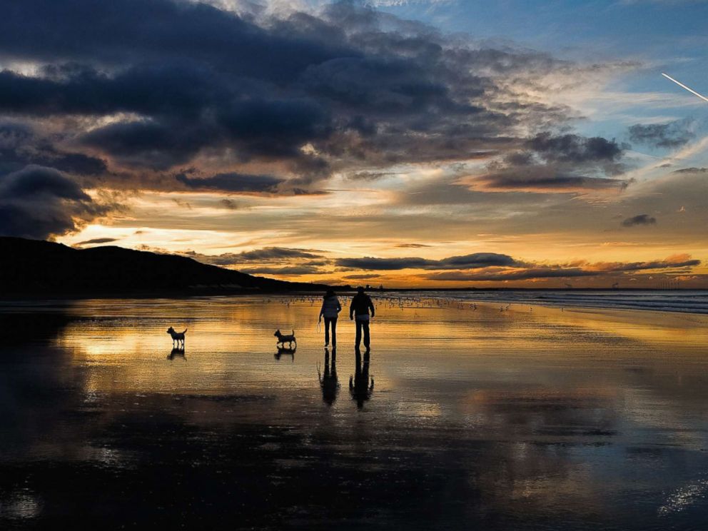 PHOTO: A couple walk their dogs on the beach as the sun sets on the Autumn Equinox, which marks the first day of Autumn, Sept. 23, 2015, in Saltburn, England.