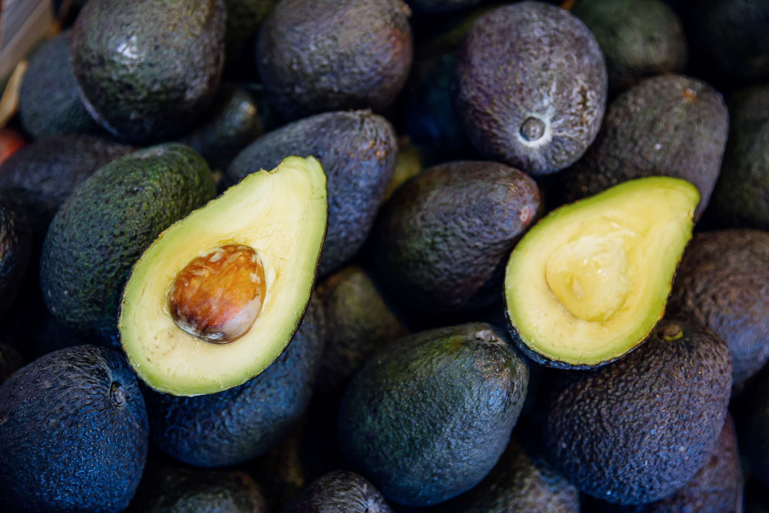 PHOTO: A freshly cut avocado lies on top of uncut avocados.