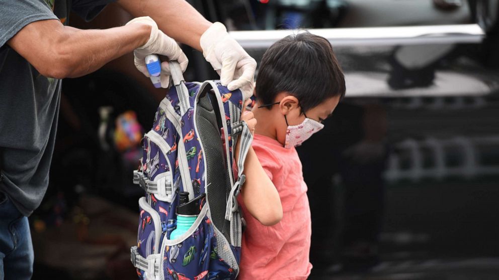 PHOTO: A staff member helps a student put on his knapsack as he arrives at STAR Eco Station Tutoring & Enrichment Center where he will follow his remote school classes, Sept. 10, 2020, in Culver City, California.