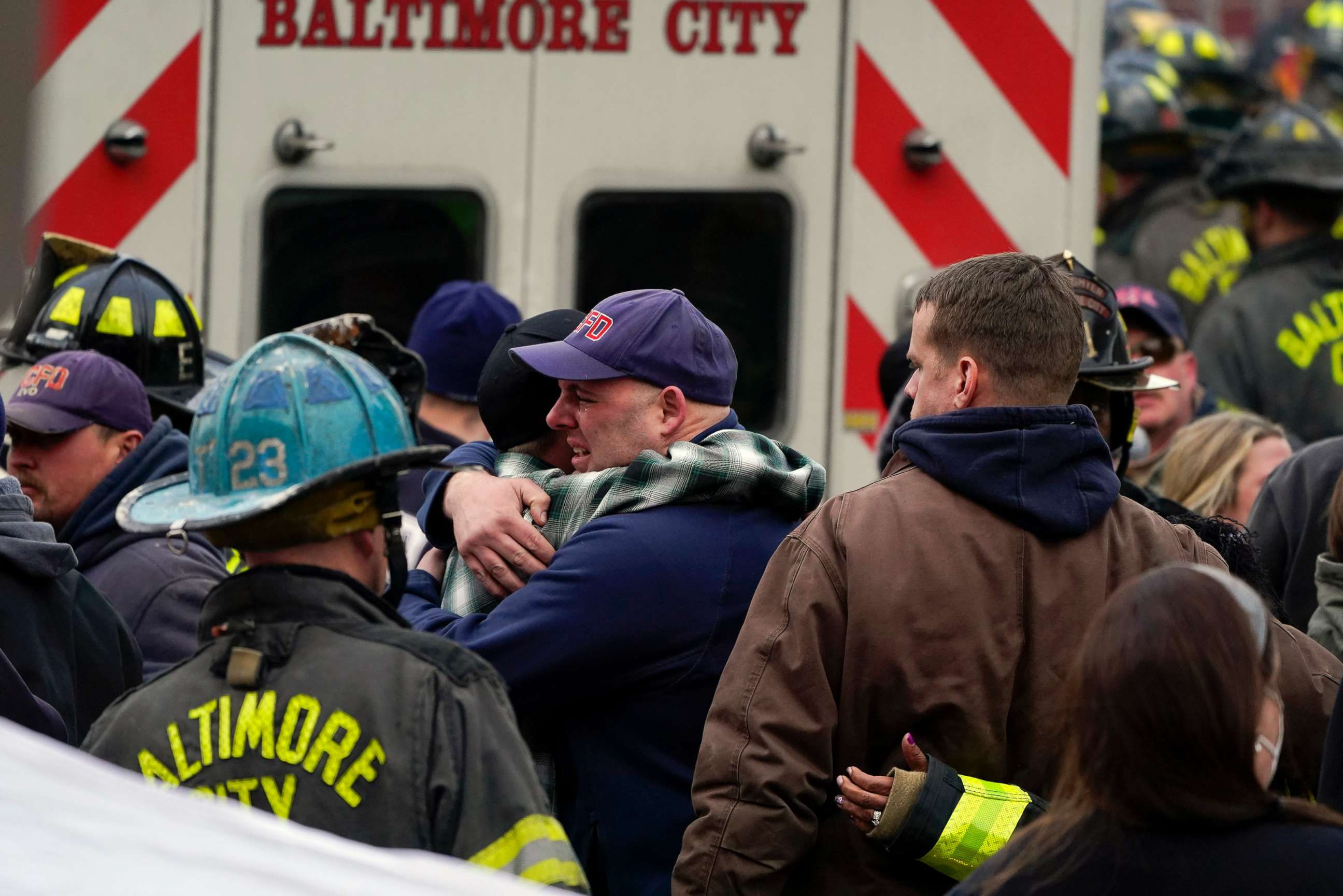 PHOTO: People embrace after a deceased firefighter was put into an ambulance following a building collapse while firefighters battled a two-alarm fire at a vacant row home, Jan. 24, 2022, in Baltimore. Three firefighters died. 