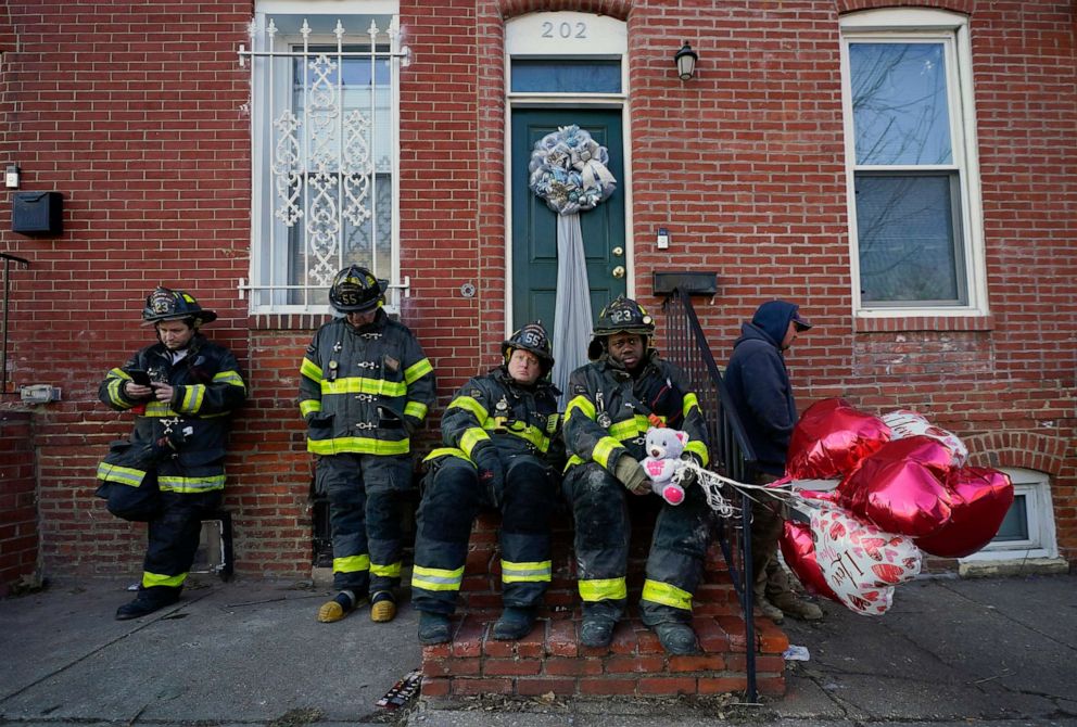 PHOTO: A Baltimore firefighter holds balloons given to him by neighbor Darlene Cucina as a group of fire officials sit on a stoop across the street where three firefighters died in a two-alarm blaze in a vacant row home, Jan. 24, 2022, in Baltimore.