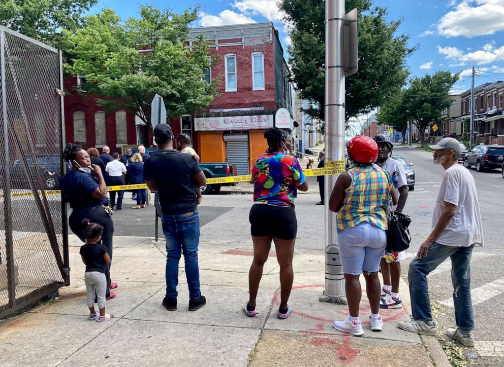 PHOTO: A cluster of people watch as Baltimore Police investigate a shooting, June 16, 2021, in Baltimore.