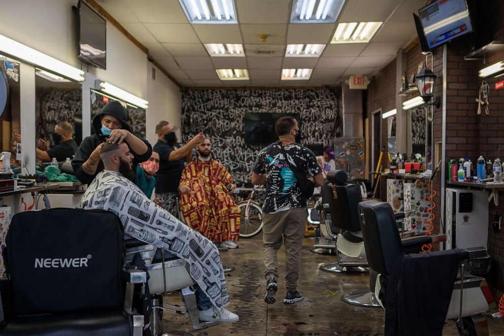 PHOTO: Barbers wearing protective masks cut hair in front of a tv showing the news during the 2020 Presidential election in Miami, Fla., Nov. 4, 2020.