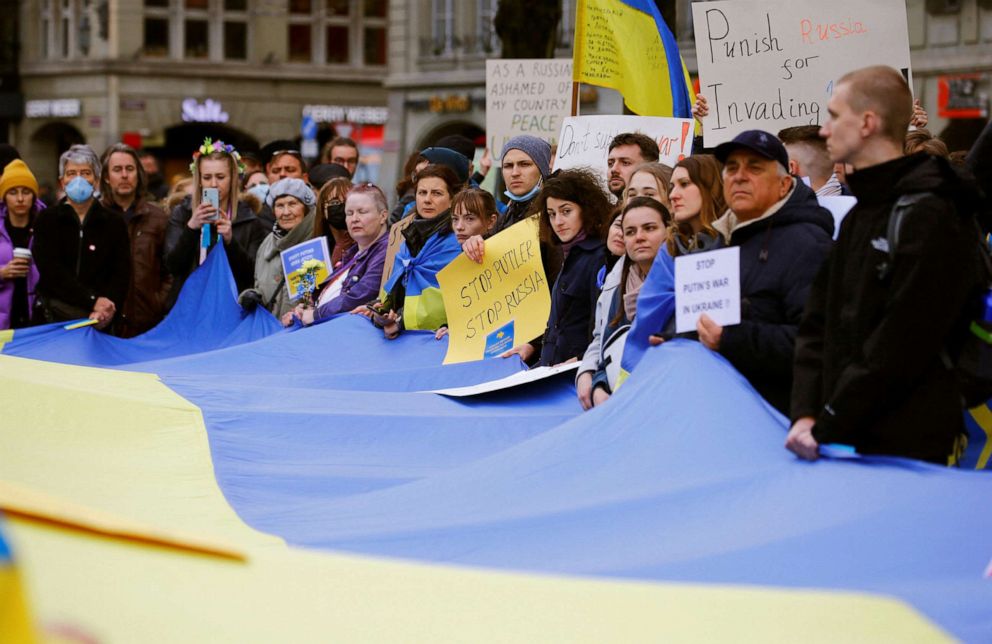 PHOTO: Ukranian people living in Switzerland display posters as they stand around a huge Ukrainian national flag during a protest in Bern, Switzerland, Feb. 24, 2022.