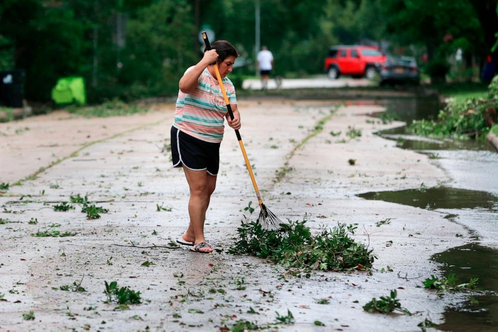 PHOTO: Resident Isabel Perez rakes up downed tree branches from the street outside of her home during a lull in the wind and rain as Tropical Storm Beryl passes, July 8, 2024, in Rosenburg, Texas.