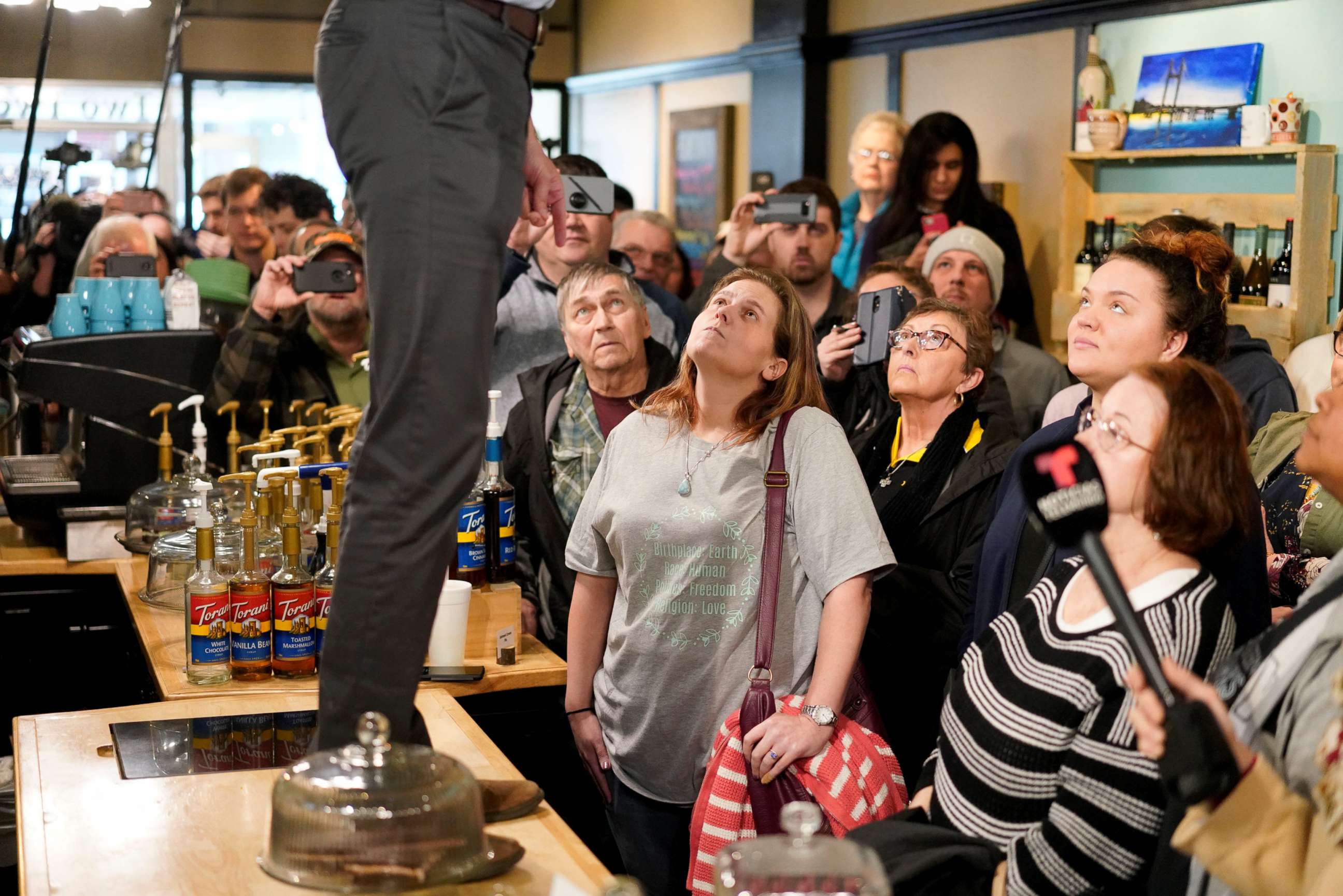 PHOTO: Attendees listen as Democratic 2020 presidential candidate Beto O'Rourke, standing on counter, speaks during a campaign stop at a coffee house in Burlington, Iowa, March 14, 2019.