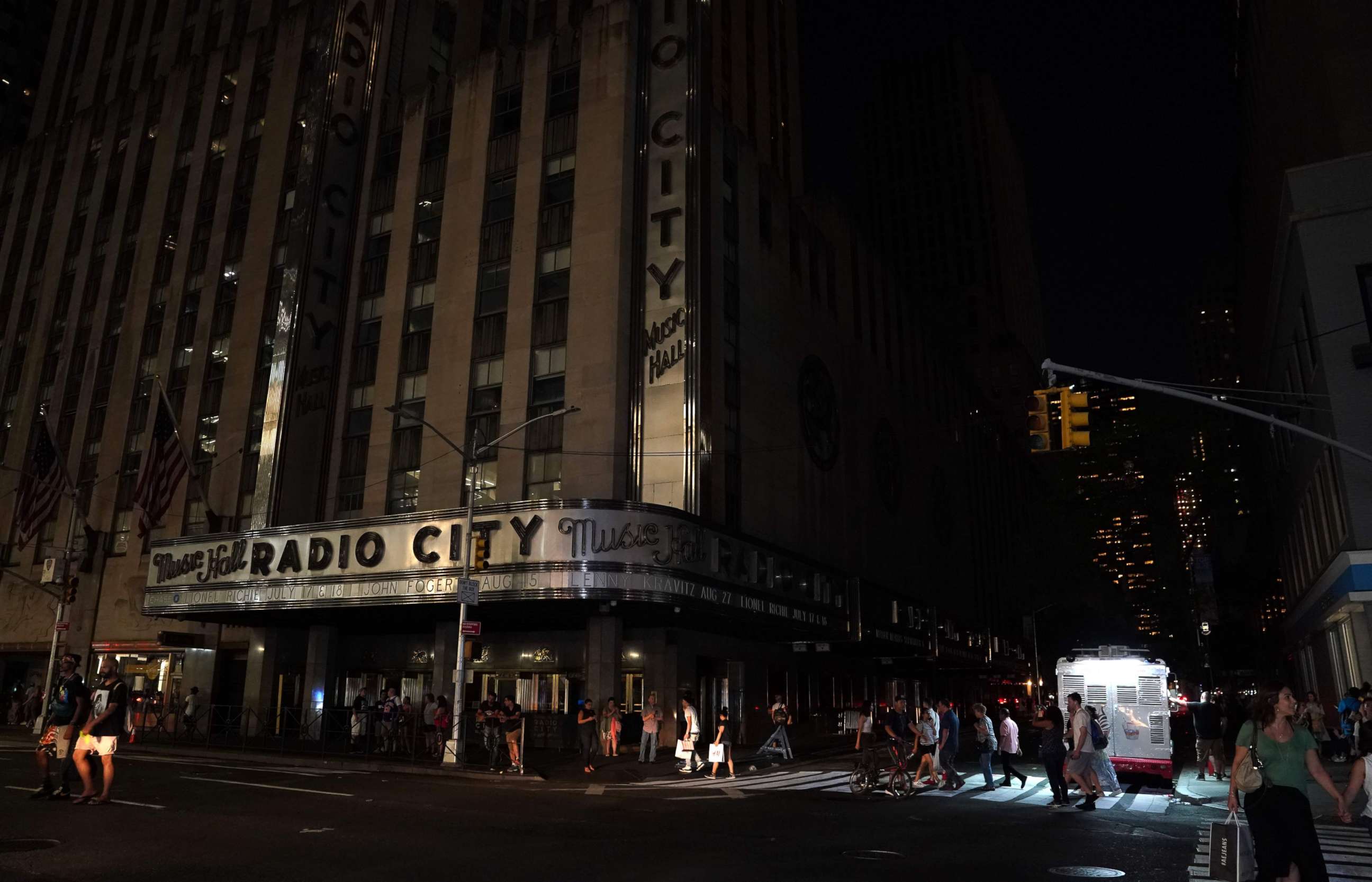 PHOTO: People walk past Radio City Music Hall in the dark during a major power outage affecting parts of New York, July 13, 2019.