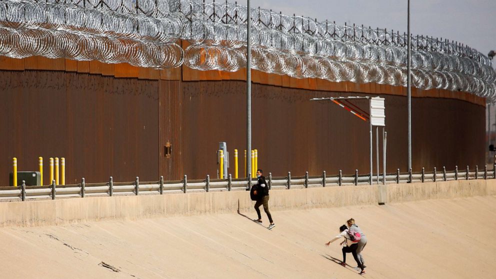 PHOTO: Asylum-seeking migrants walk near the border wall after crossing the Rio Bravo river to turn themselves in to U.S Border Patrol agents to request asylum in El Paso, Texas, as seen from Ciudad Juarez, Mexico, March 30, 2022. 
