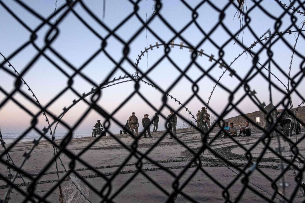 PHOTO: Central American migrants -travelling in a caravan- sit next to US border patrol officers after crossing the Mexico-US border fence to San Diego County, as seen from Playas de Tijuana, Baja California state, Mexico, Dec. 13, 2018. 